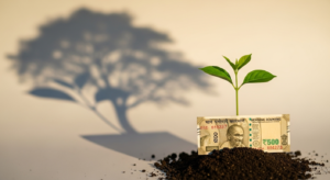 A visual metaphor for the power of compounding: a tiny sapling, nurtured by a 500 Rupee note, casts a large shadow of a mature tree, representing small investments growing into significant wealth over time with the power of compounding